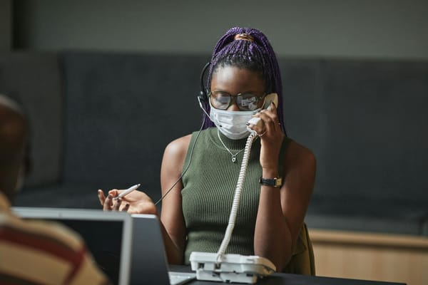 Woman with purple braided hair on a call in an office, wearing a mask for safety.